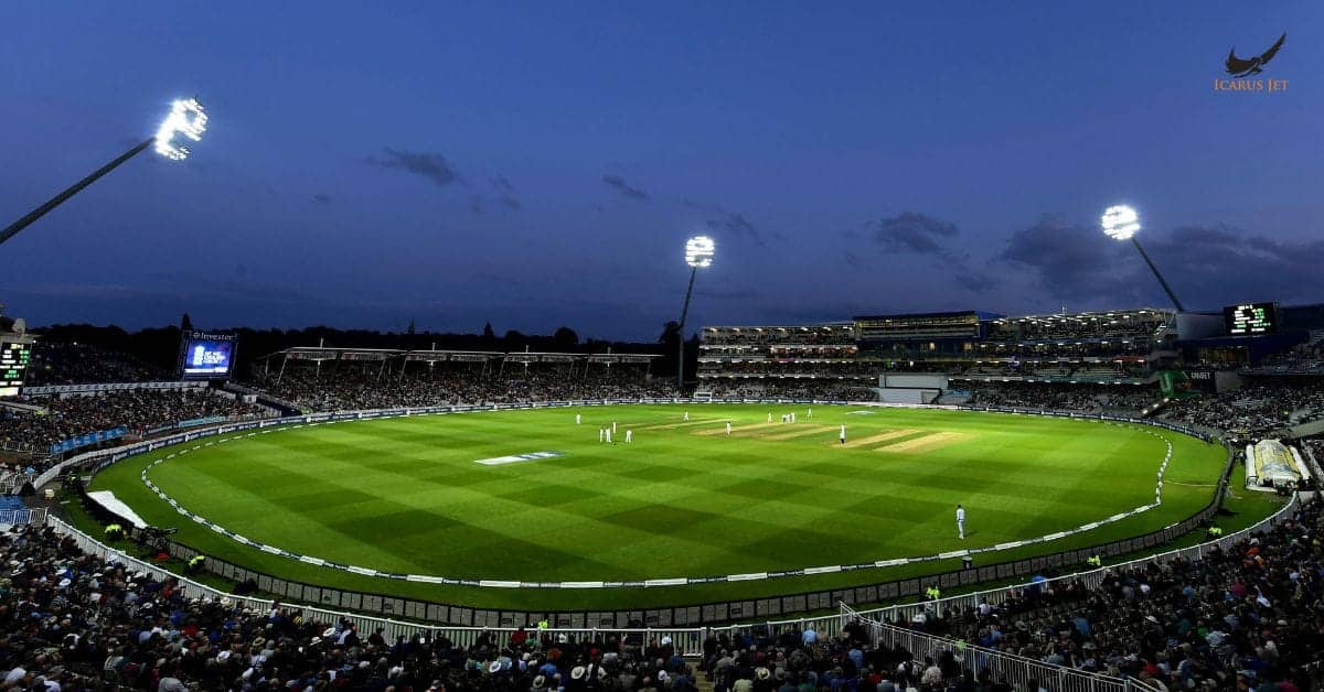 Modern private jet parked at a stadium during a cricket match at night.