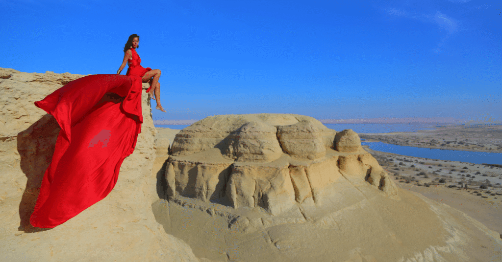 Sharm El Sheikh International Airport (SSH / HESH): woman in a flowing red dress seated on desert cliffs overlooking water