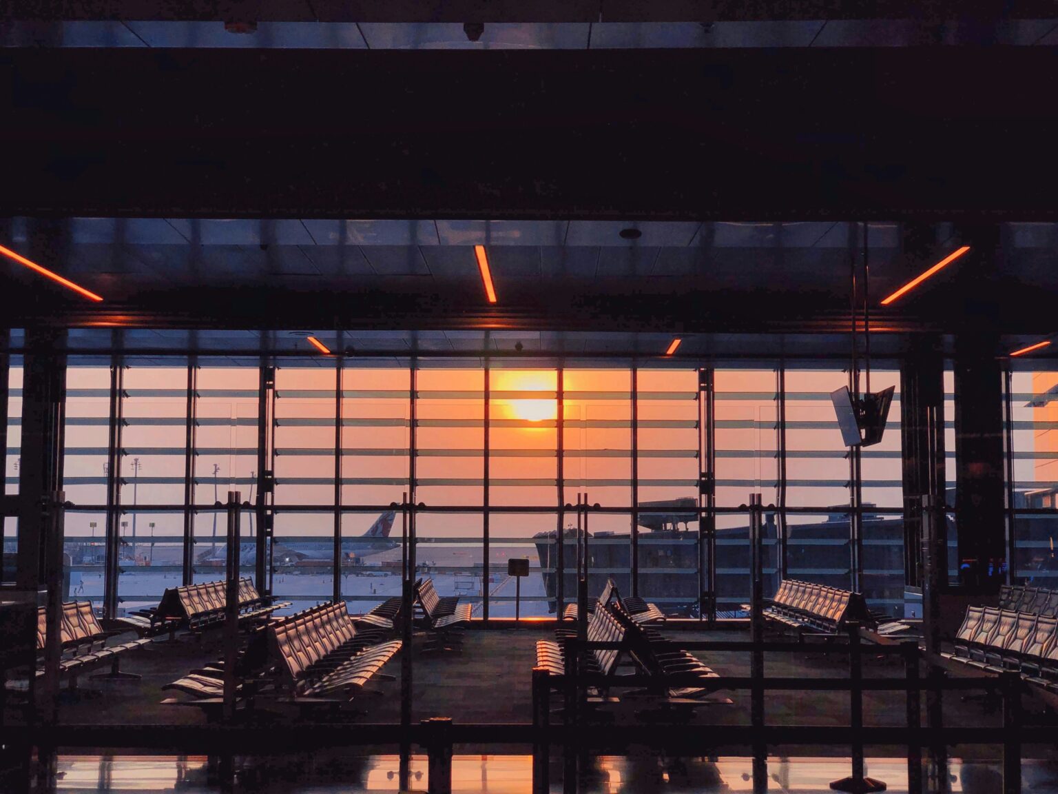 Al Maktoum International Airport (DWC / OMDW): airport terminal departure lounge at sunset with empty seating and a wall of windows